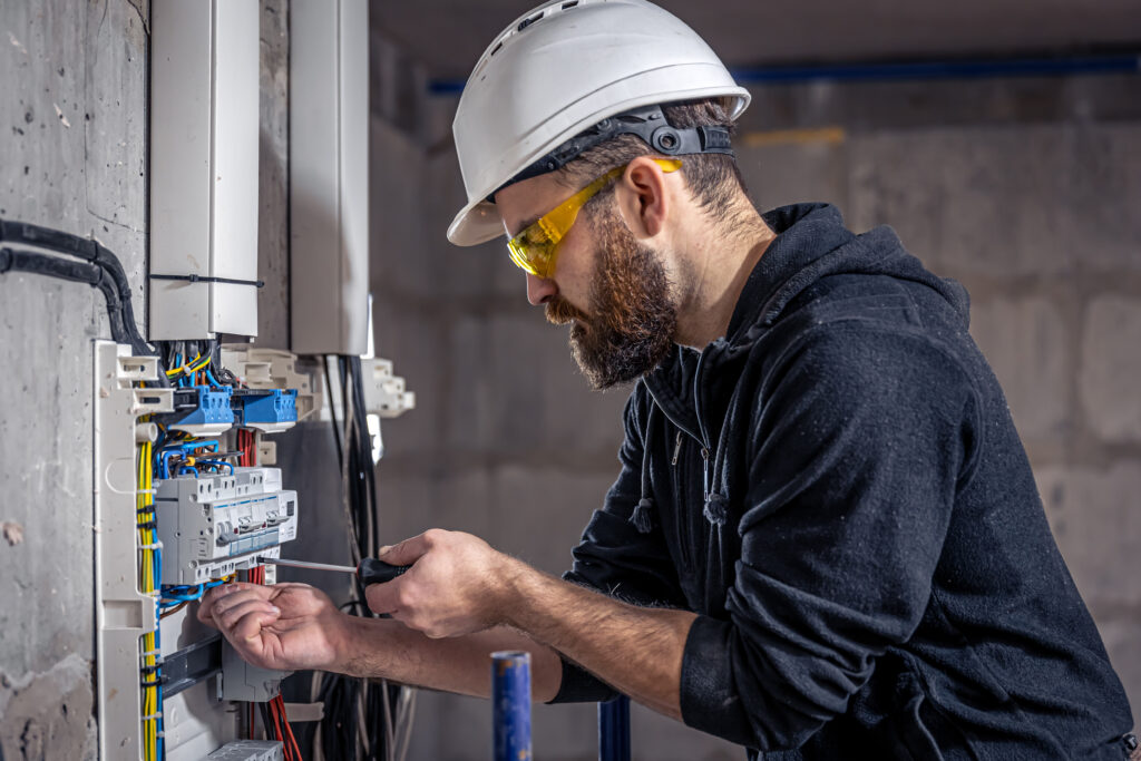 a male electrician works in a switchboard with an electrical connecting cable.